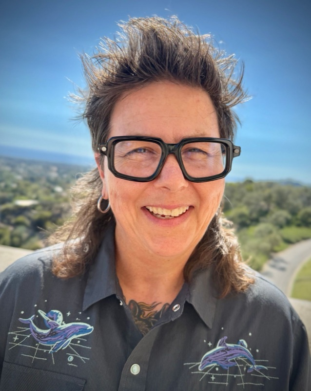 Christy Schaefer smiling outdoors, with green hills and the ocean behind